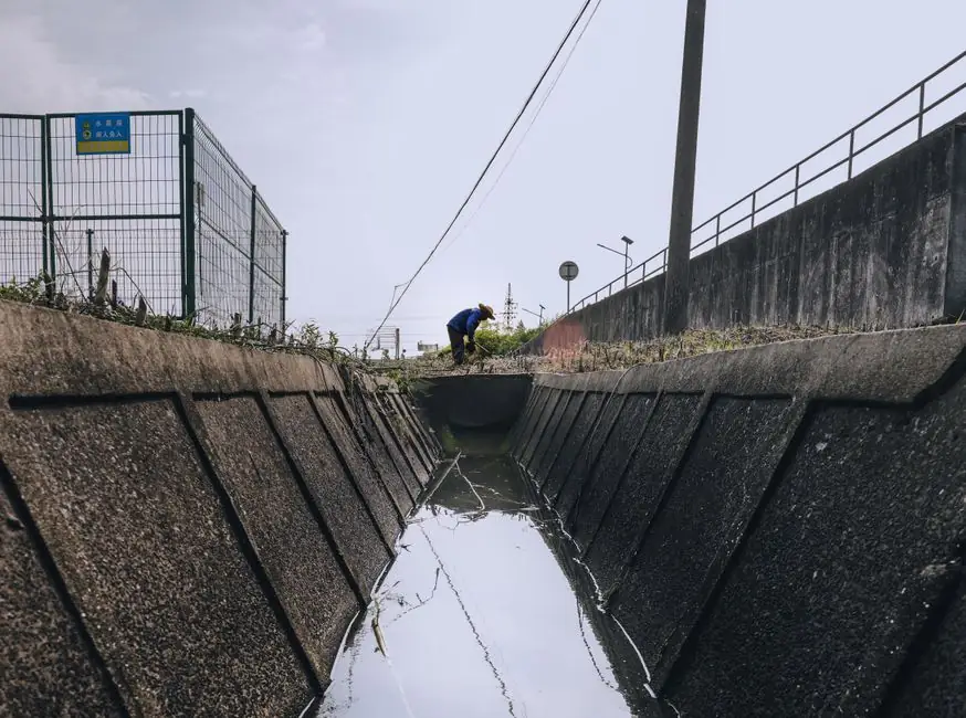 A person in blue attire working near a large drainage channel on a clear day.